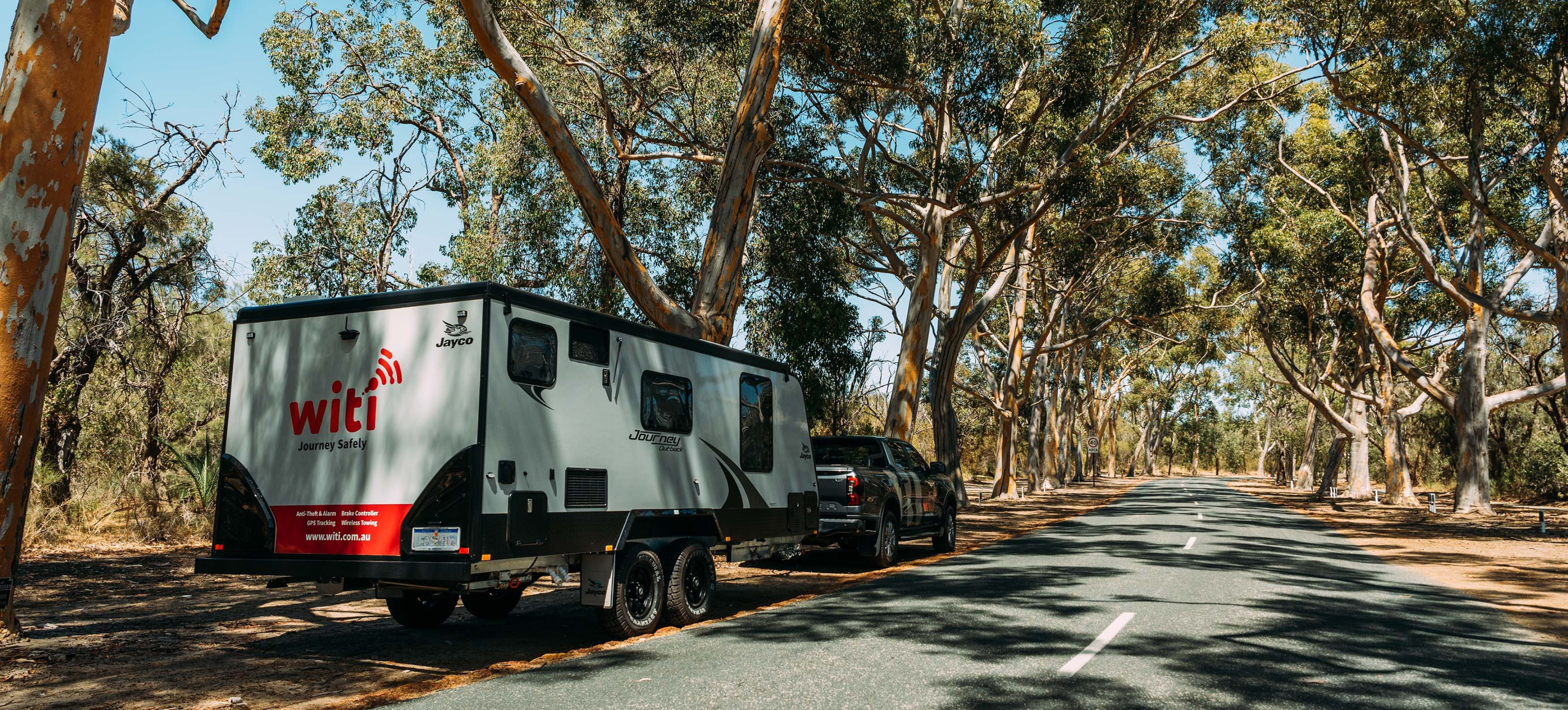 Caravan with a WiTi logo parked on a road surrounded by trees